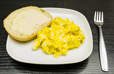 Scrambled eggs and a slice of bread with butter on a white plate.