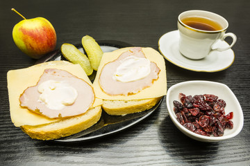 Plate with a slice of bread with ham, cheese and mayonnaise, for this cucumber, and an apple and a bowl of dried cranberries. Drinking a cup of tea.