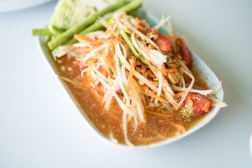 papaya salad, spicy papaya salad with salted crab and fermented fish, in white dish in the table. Famous Thai food, papaya salad or what we called 