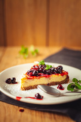 Beautiful traditional italian cheesecake with red fruits, mint, and powdered sugar on wooden background, selective focus