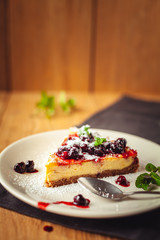 Beautiful traditional italian cheesecake with red fruits, mint, and powdered sugar on wooden background, selective focus