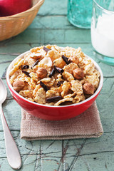 Corn flakes with hazelnuts and chocolate  in red bowl for breakfast on old cyan wooden table