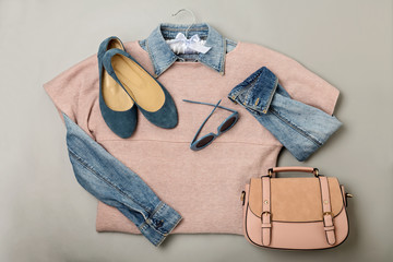 Flat lay of a casual woman fashion outfit - jeans, pink dress, handbag and sunglsses. Top view on gray background.
