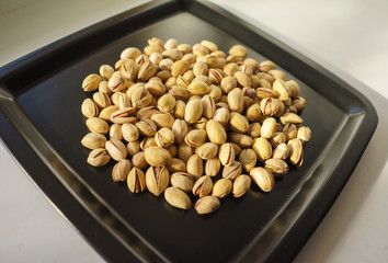 Pistachio nuts, a bunch on a black plate. A close-up photograph. Unrefined whole kernel 