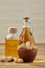 Fototapeta na wymiar Aromatic oil in a glass jar and bottle with peanuts in bowl on wooden table, close-up.