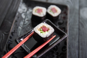Hand using chopsticks pick. Maki-Sushi, tuna-maki rolls in front of face of young man. Fresh made Sushi set with tuna, cheese and cucumber. Traditional Japanese cuisine.