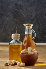 Fototapeta na wymiar Aromatic oil in a glass jar and bottle with peanuts in bowl on wooden table, close-up, vertical