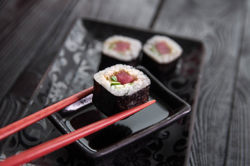 Hand using chopsticks pick. Maki-Sushi, tuna-maki rolls in front of face of young man. Fresh made Sushi set with tuna, cheese and cucumber. Traditional Japanese cuisine.