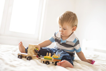 Little adorable boy playing with wooden train toy in bedroom