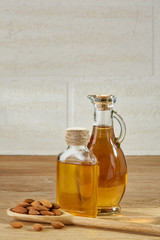 Aromatic oil in a glass jar and bottle with almond in a scoop on wooden table, close-up.