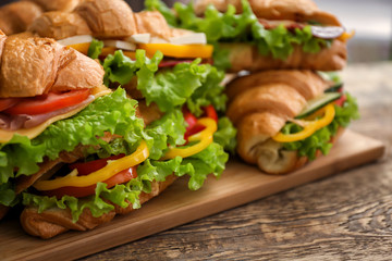 Wooden board with delicious croissant sandwiches on table