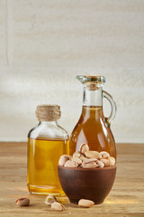 Aromatic oil in a glass jar and bottle with pistachios in bowl on wooden table, close-up.