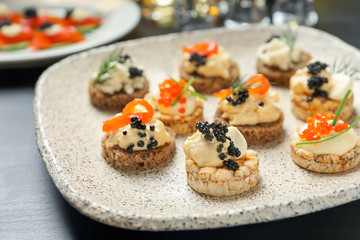 Delicious canapes with black and red caviar on plate, closeup