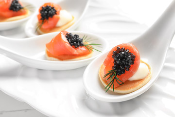Tasty appetizers with black caviar and salmon in ceramic spoons on plate