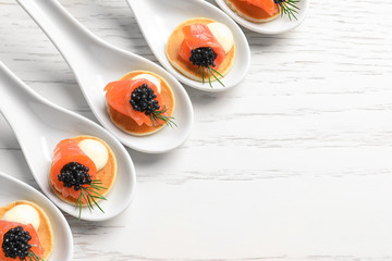 Tasty appetizers with black caviar and salmon in ceramic spoons on table