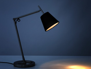 Stylish desk lamp on table in darkness