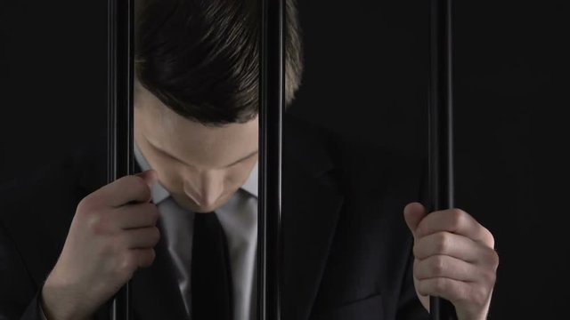 Young corrupt businessman in prison cell closeup, feeling guilty and regret