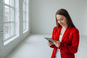 Portrait of smiling successful adult girl in red jacket looking at her tablet