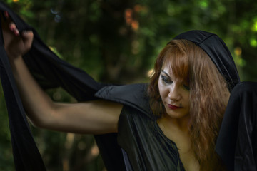 young witch from legends and fairy tales performs a sorcerous rite in the forest.