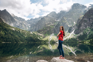 Young beautiful and smiling girl standing on the shore of the lake and admire the mountain scenery in Poland
