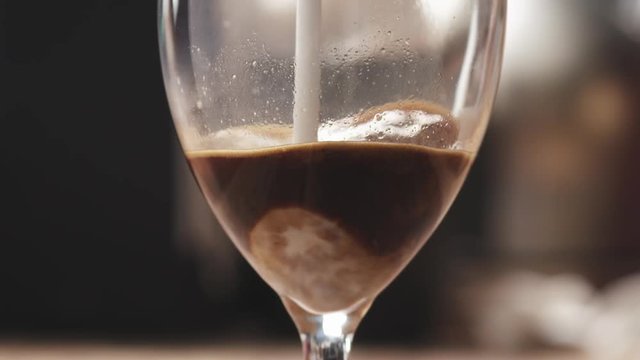 Slow motion closeup of pouring steamed milk into coffee in glass