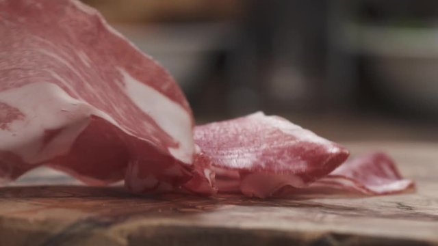 Slow motion of Italian coppa ham falling on wood board closeup
