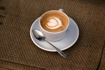 Cappuccino mit Milchschaum in Herzform in Tasse auf Hintergrund Sackleinen