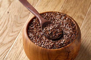 Flax seeds in wooden bowl and spoon on rustic wooden background, top view, shallow depth of field