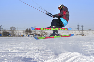 A male athlete engaged in snow kiting on the ice of a large snowy lake. He performs the jump. Winter sunny frosty day. Close-up.