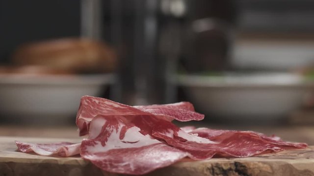 Slow motion of Italian coppa ham falling on wood board closeup