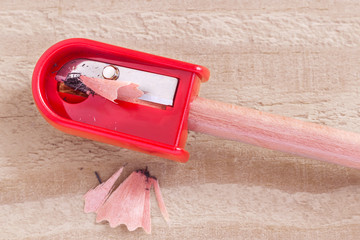 Red pencil-sharpener and pencil isolated on brown wooden background.