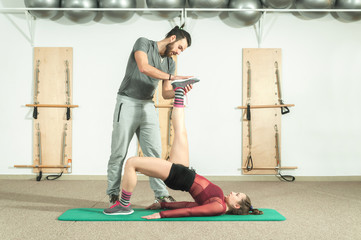 Handsome male personal trainer with a beard helping young beautiful girl for aerobic exercise in...