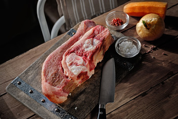 Raw beef with bone on wooden board and table. Beef-infusion broth ingredients. With knife, salt and pepper.