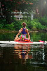 Fototapeta premium Young athletic woman doing fitness on a board with an oar on a lake