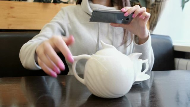 Unrecognizable woman's hands pictures of teapot and Cup in a cafe on her cell phone.