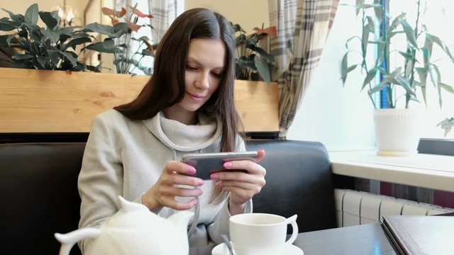 Young woman brunette pictures of teapot and Cup in a cafe on her cell phone.