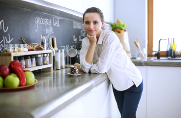 Portrait of young woman standing against kitchen background.