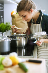 Young woman standing by the stove in the kitchen .