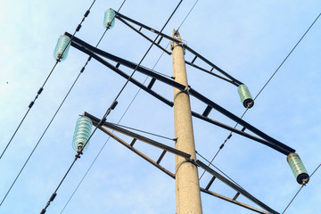Supports high-voltage power lines against the blue sky with clouds. Electrical industry.