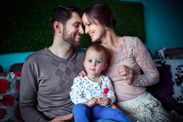 Obraz premium a small daughter sits at her young parents knees. happy family concept