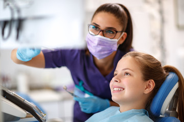 Child in dental chair with female dentist looking at dental footage - obrazy, fototapety, plakaty