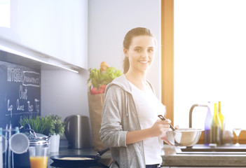 Young woman prepares pancakes in the kitchen while standing near the table. Woman in the kitchen. Cooking at kitchen.