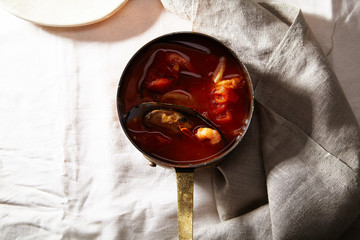Traditional mediterranean soup bouillabaisse with mussels, shrimps, tomatoes and fish broth served in copper saucepan on linen tablecloth. Holiday meal concept
