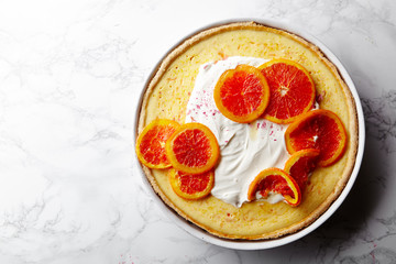 Cheesecake with caramelized red oranges and whipped cream on white marble table