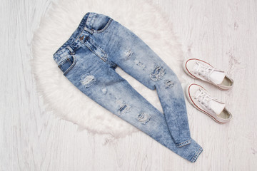 Blue ragged  jeans and white sneakers on white fur. Fashionable concept