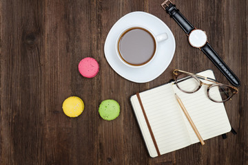 Fototapeta na wymiar Top view on cup of coffee, macarons, notebook, watch and glasses. Wooden background
