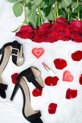 Black shoes and a bouquet of red roses on a white fur. Red candles, lipstick
