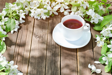Mug of tea among apple flowers on a wooden background.