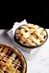 Pie crust design ideas - various ways of pie decoration with lattice and leaves. Apple, strawberry and raspberry pies cooked and served with tea on white marble table