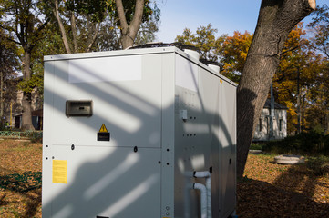 Gray commercial cooling unit for central ventilation standing outdoor on the ground covered by...